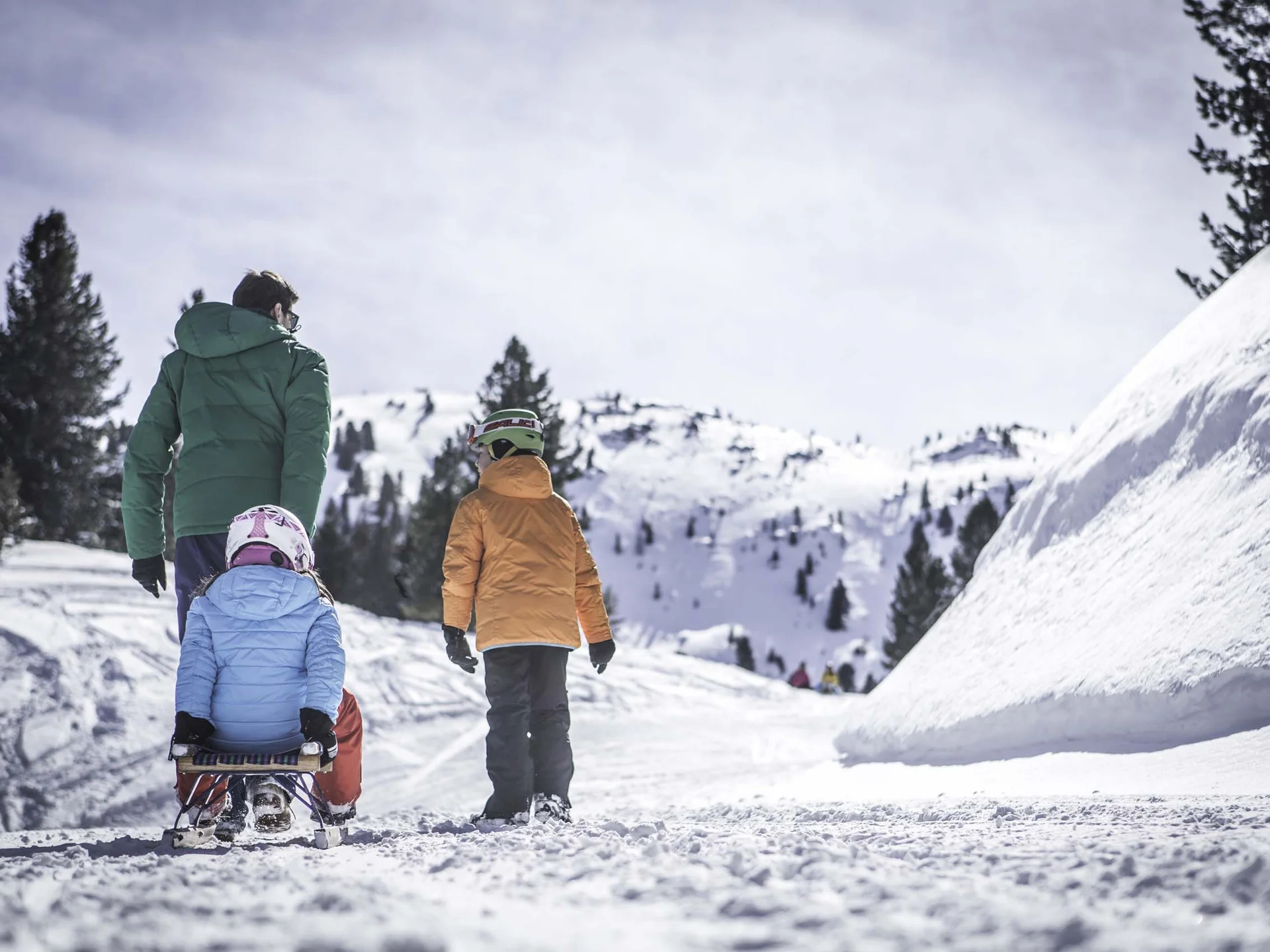 Der Lodenwirt in Vintl | Hotel, Residence & Restaurant Familie mit Kind auf einem Schlitten auf einem verschneiten Bergweg
