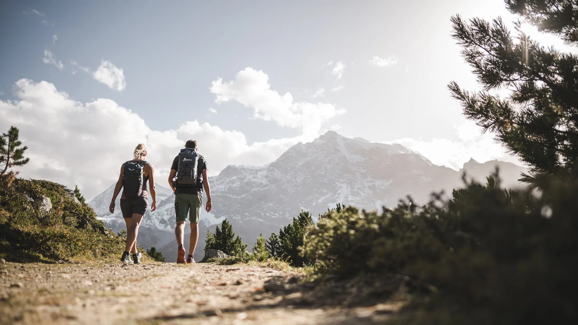 Der Lodenwirt in Vintl | Hotel, Residence & Restaurant Zwei Wanderer mit Rucksäcken auf Bergweg vor schneebedeckten Gipfeln