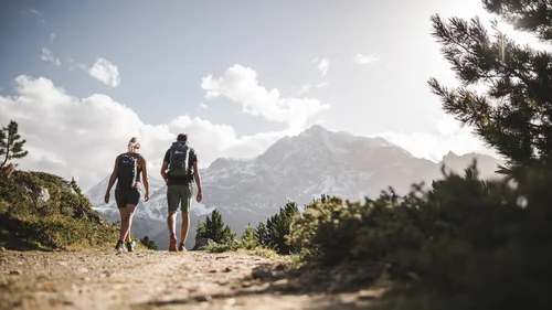Der Lodenwirt in Vintl | Hotel, Residence & Restaurant Zwei Wanderer mit Rucksäcken auf Bergweg vor schneebedeckten Gipfeln