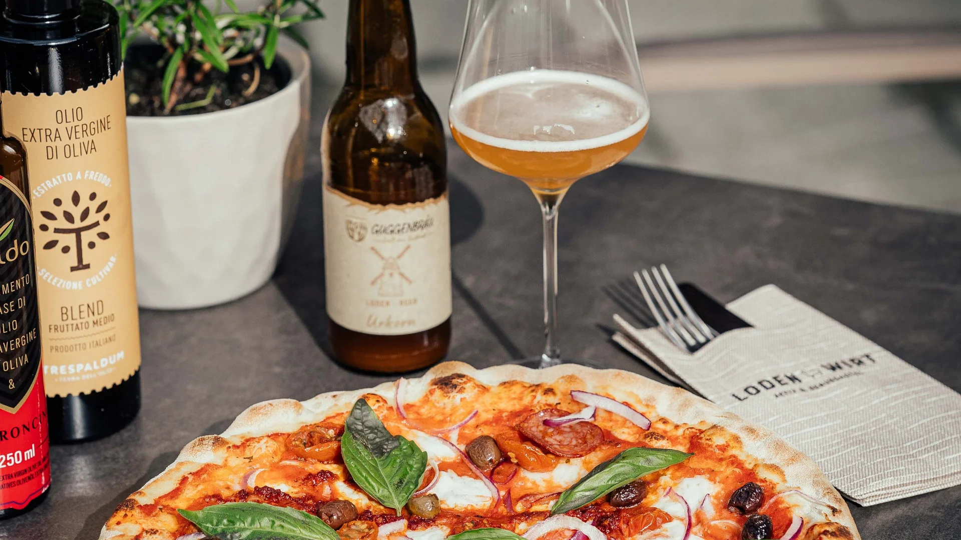Der Lodenwirt in Vintl | Hotel, Residence & Restaurant Pizza mit Basilikum, Olivenöl, Bierflasche und Glas auf Tisch im Freien