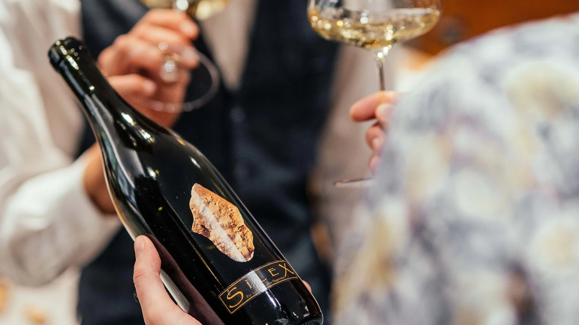Der Lodenwirt in Vintl | Hotel, Residence & Restaurant Person hält Weinflasche, andere riecht an Weinglas mit Weißwein