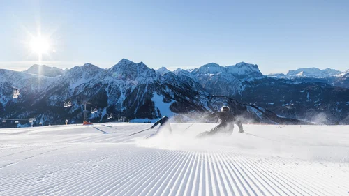Der Lodenwirt in Vintl | Hotel, Residence & Restaurant Skifahrer auf präparierter Piste vor verschneiten Bergen und Sessellift