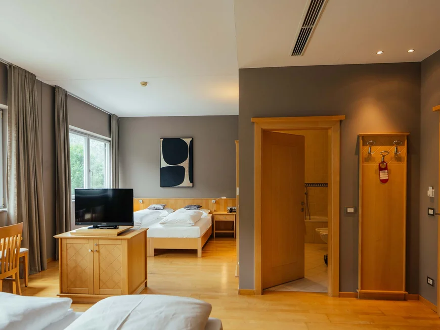 Der Lodenwirt in Vintl | Hotel, Residence & Restaurant Helles Hotelzimmer mit Doppelbett, Fernseher, Esstisch und offenem Badezimmer