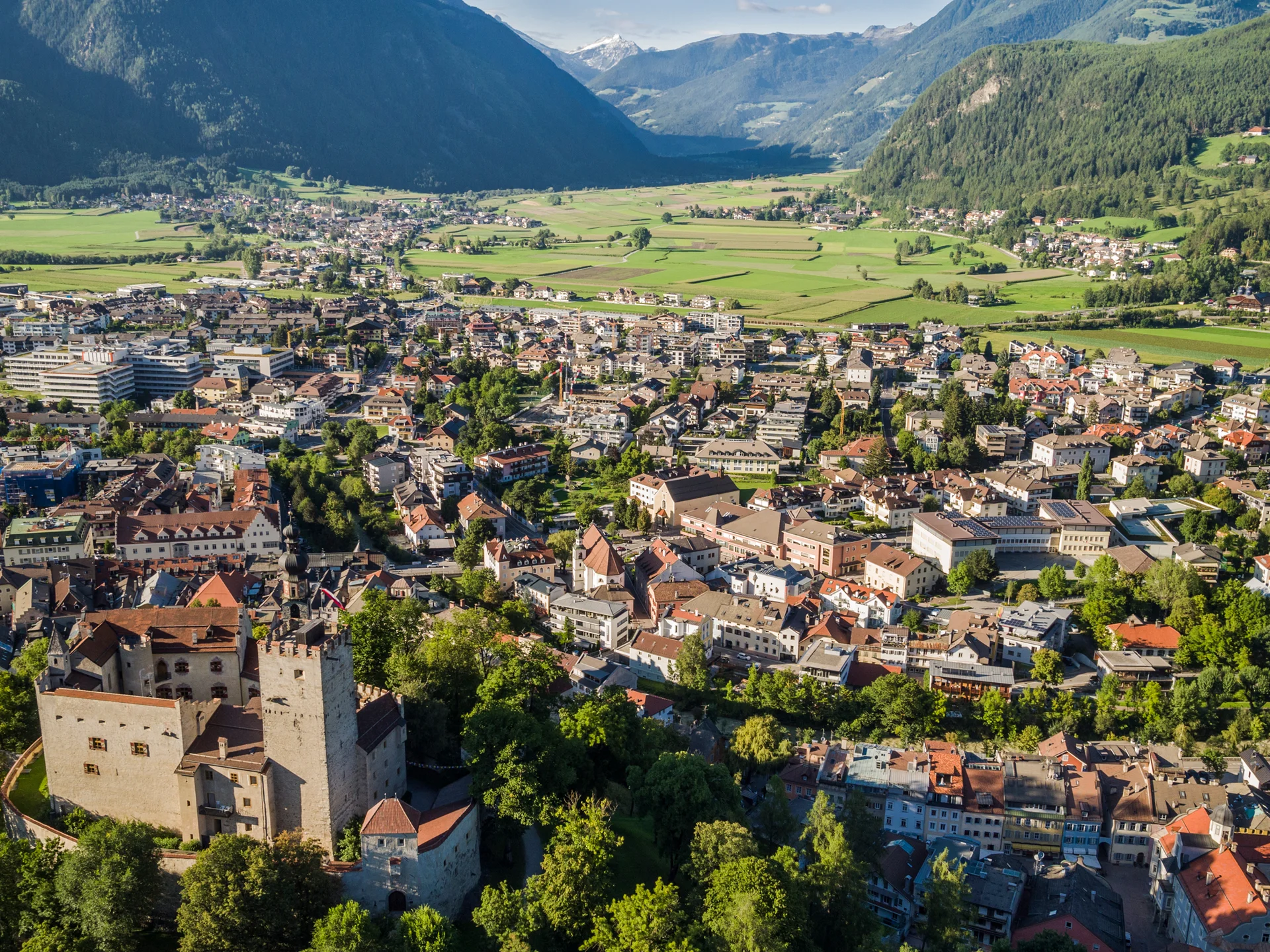 Der Lodenwirt in Vintl | Hotel, Residence & Restaurant Luftaufnahme einer Stadt mit Schloss und Bergen im Hintergrund