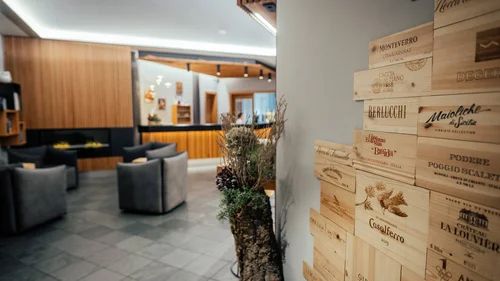 Der Lodenwirt in Vintl | Hotel, Residence & Restaurant Moderne Hotellobby mit grauen Sesseln und Holzwanddekoration