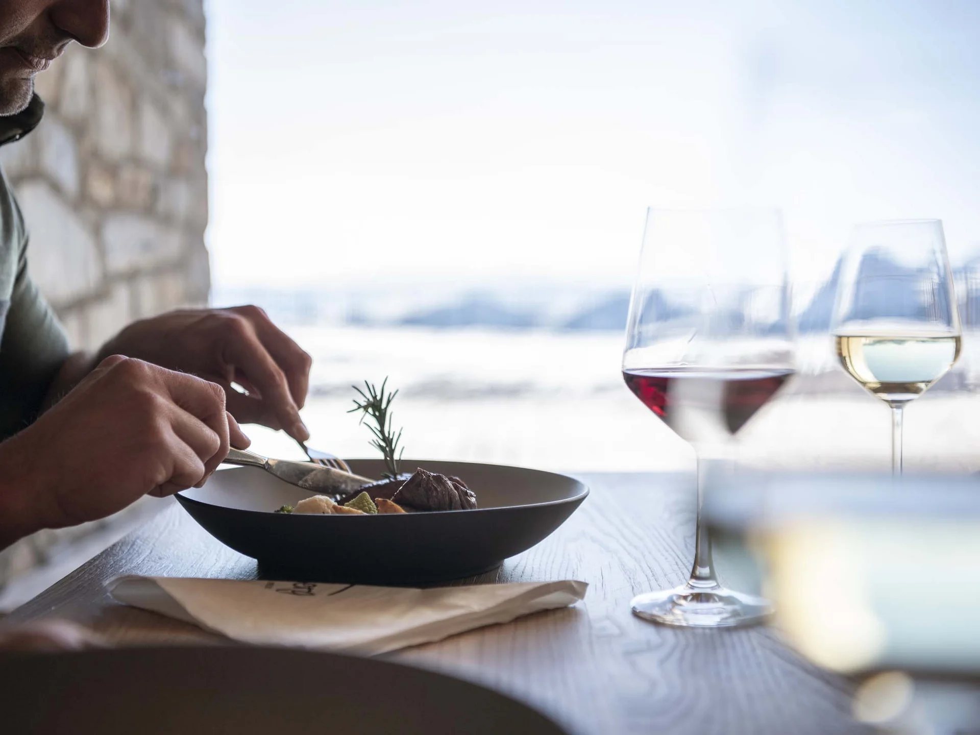 Der Lodenwirt in Vintl | Hotel, Residence & Restaurant Gast genießt ein Gericht mit zwei Gläsern Wein an einem Fenster