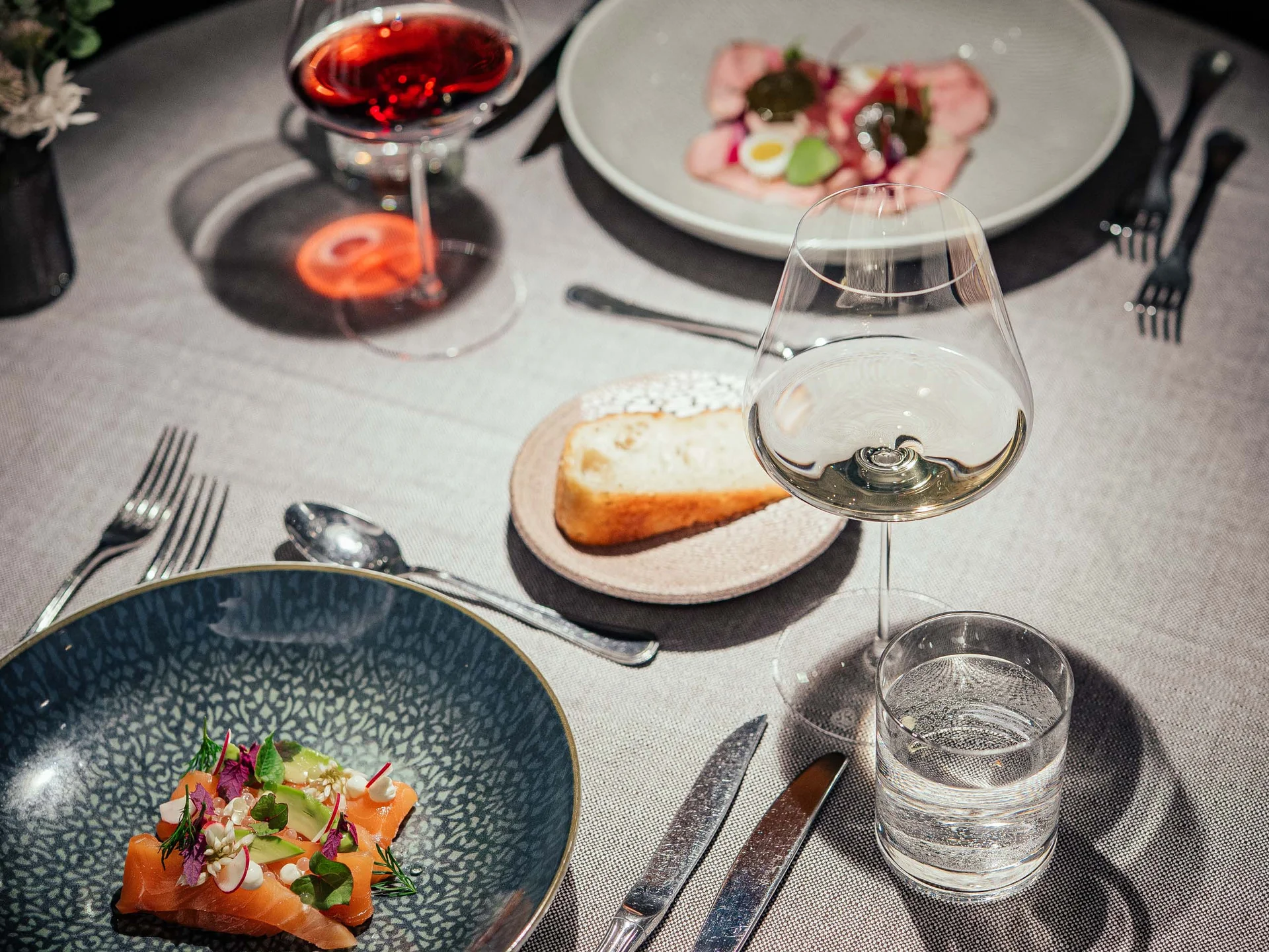 Der Lodenwirt in Vintl | Hotel, Residence & Restaurant Fein gedeckter Tisch mit zwei Gängen, Rot- und Weißwein, Wasser und Brot