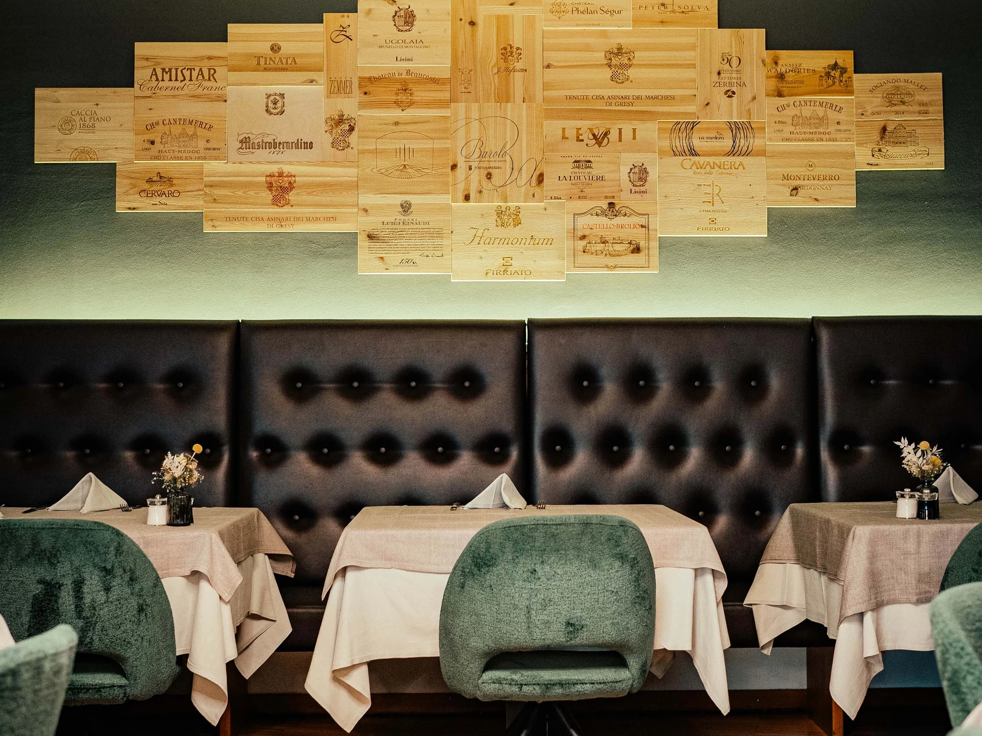 Der Lodenwirt in Vintl | Hotel, Residence & Restaurant Gemütlicher Restaurantbereich mit grünen Stühlen und Wanddekoration aus Weinkisten