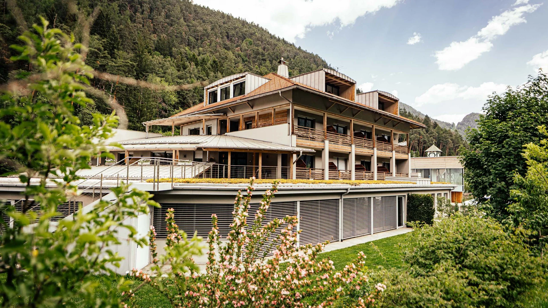 Der Lodenwirt in Vintl | Hotel, Residence & Restaurant Modernes Hotelgebäude mit Balkonen in grüner Berglandschaft