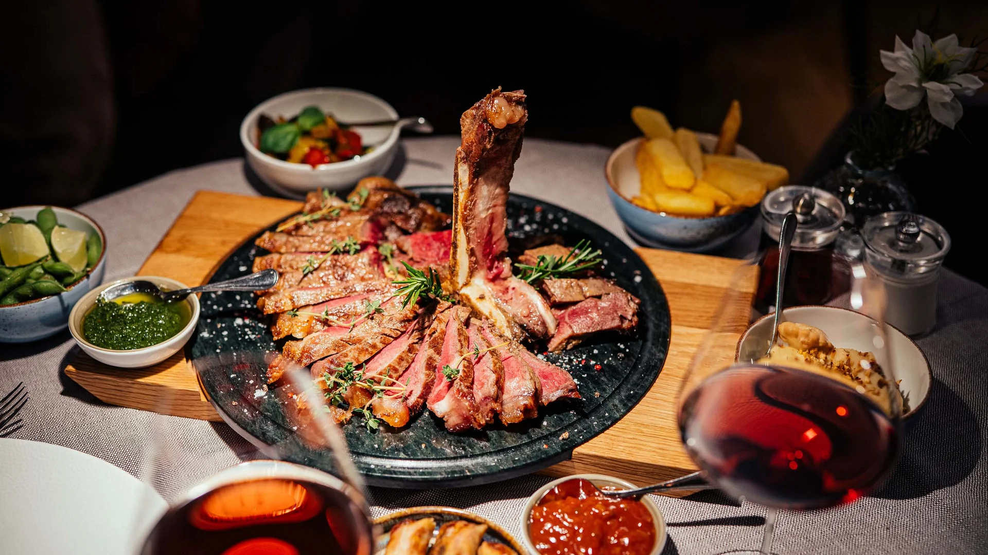 Der Lodenwirt in Vintl | Hotel, Residence & Restaurant Gegrilltes Steak mit Beilagen und Rotwein auf einem gedeckten Tisch