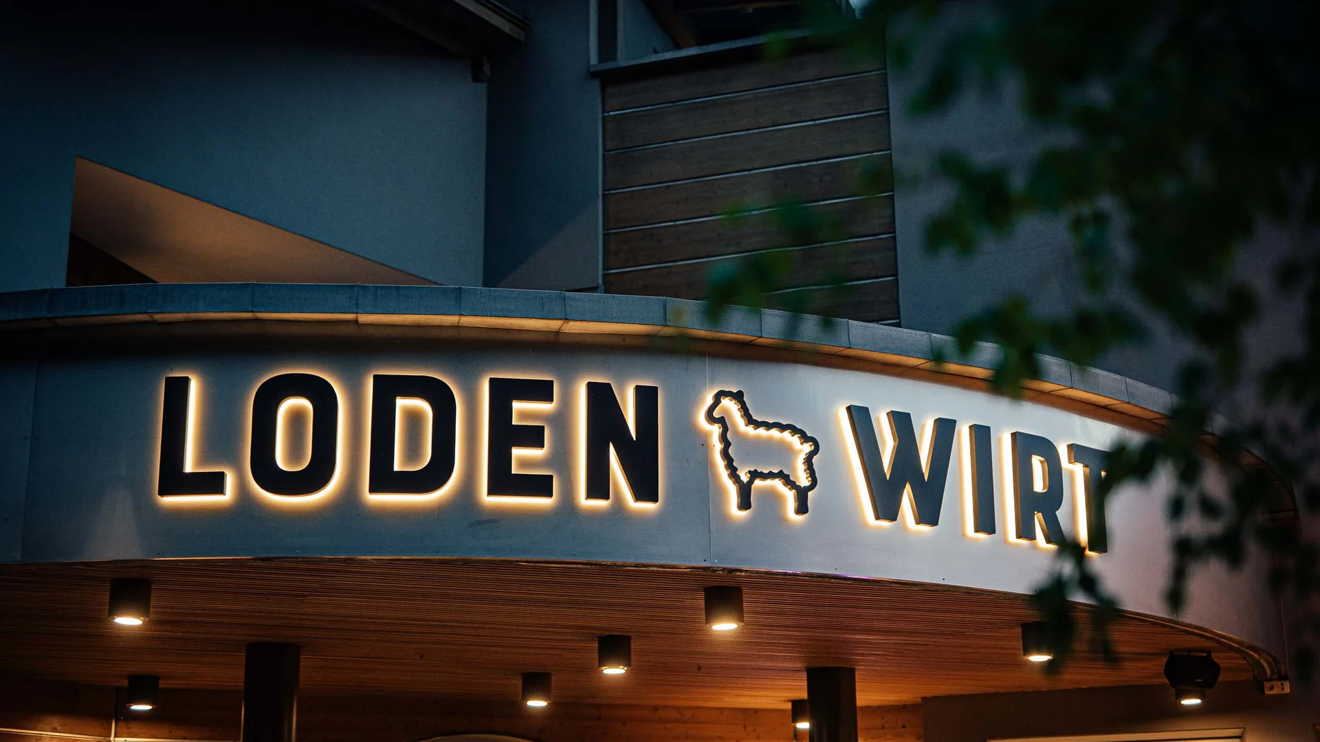 Der Lodenwirt in Vintl | Hotel, Residence & Restaurant Nächtliche Außenansicht mit beleuchtetem Schriftzug LODEN WIRT und Schafsymbol