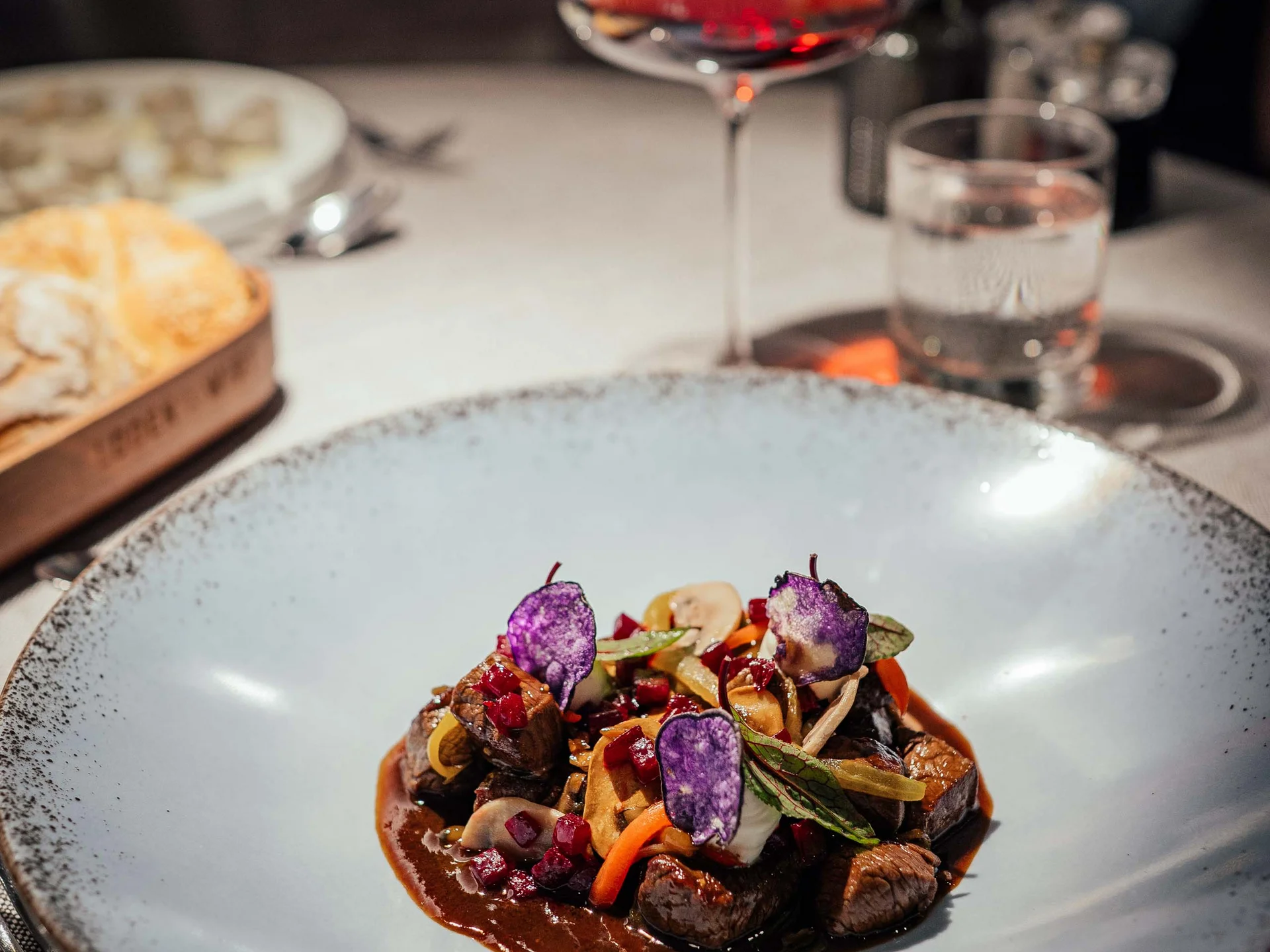 Der Lodenwirt in Vintl | Hotel, Residence & Restaurant Gourmetgericht mit Fleisch, Gemüse und violetten Chips auf weißem Teller