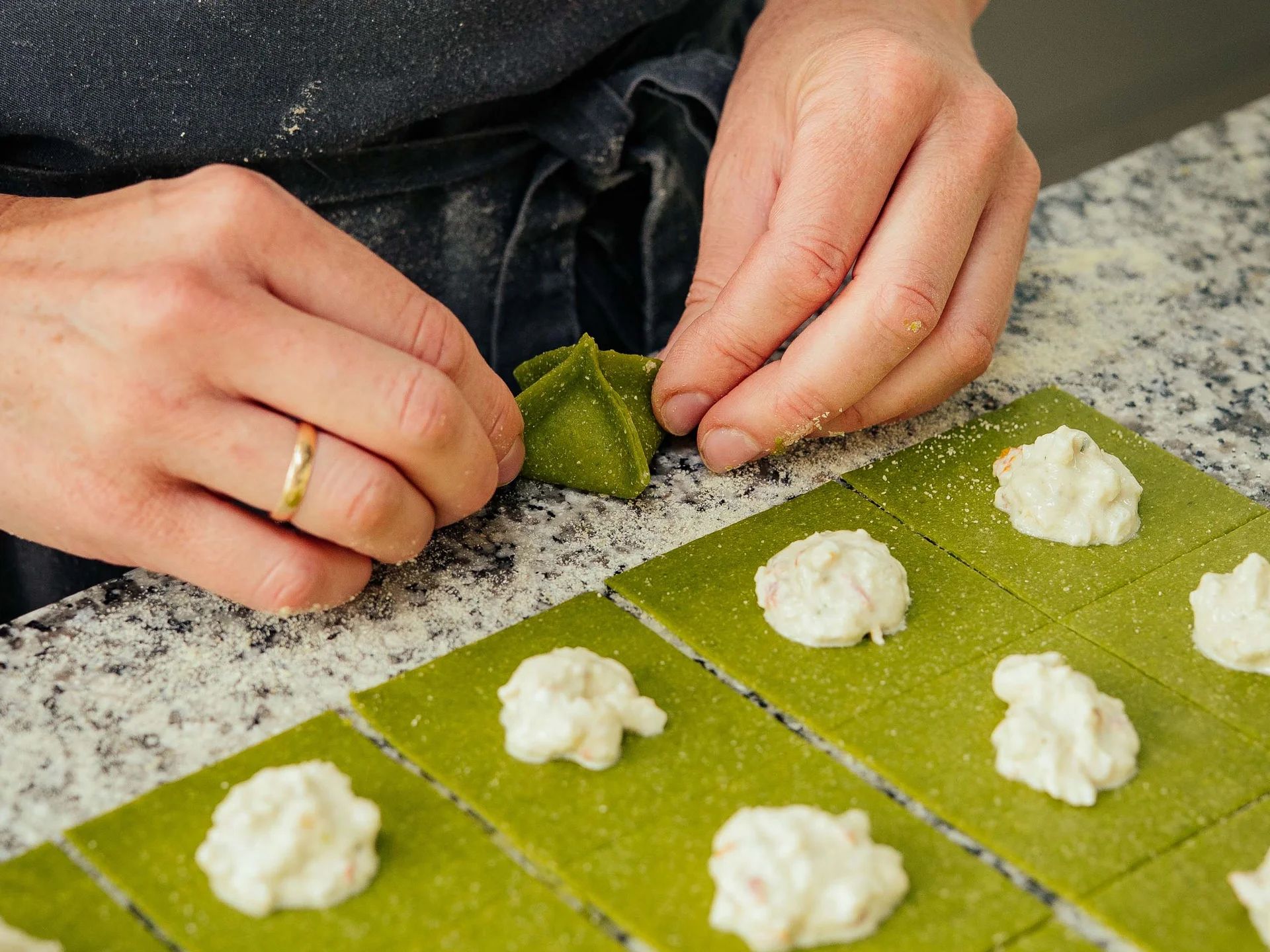 Der Lodenwirt in Vintl | Hotel, Residence & Restaurant Hände formen grüne Teigquadrate mit weißer Füllung zu Pasta